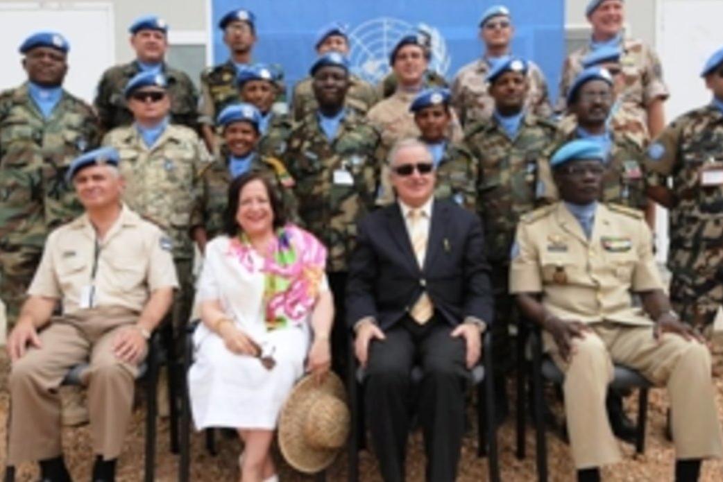 Group photo of peacekeeping personnel in military uniforms and blue berets, seated and standing in rows in front of a UN backdrop.